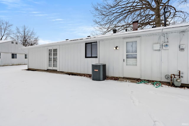 snow covered rear of property with a chimney, central AC unit, and board and batten siding