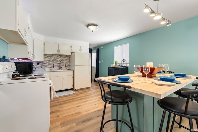 kitchen featuring white appliances, white cabinets, a sink, light wood-type flooring, and backsplash