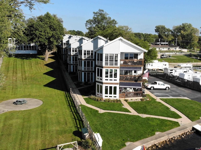 rear view of property with uncovered parking, fence, a deck, and a lawn