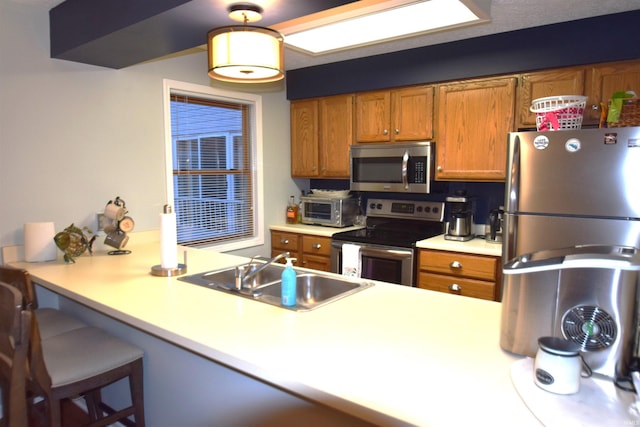 kitchen featuring brown cabinets, light countertops, appliances with stainless steel finishes, a sink, and a peninsula