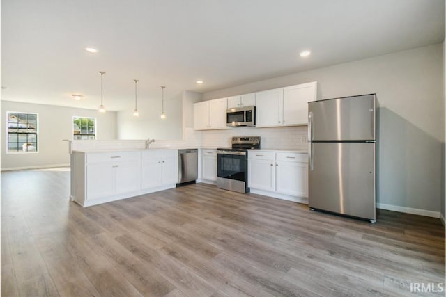 kitchen with stainless steel appliances, a peninsula, white cabinetry, light wood-type flooring, and backsplash