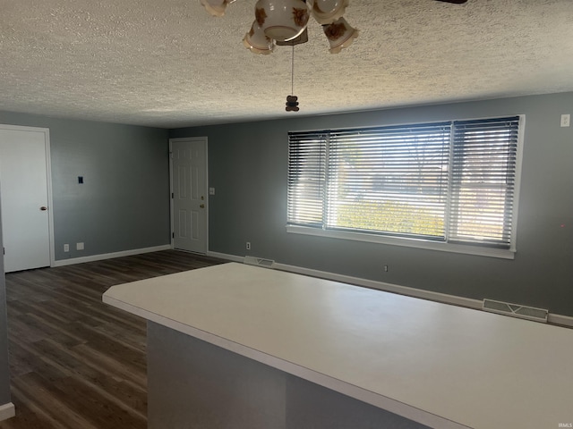 interior space with dark wood-type flooring, visible vents, a textured ceiling, and baseboards