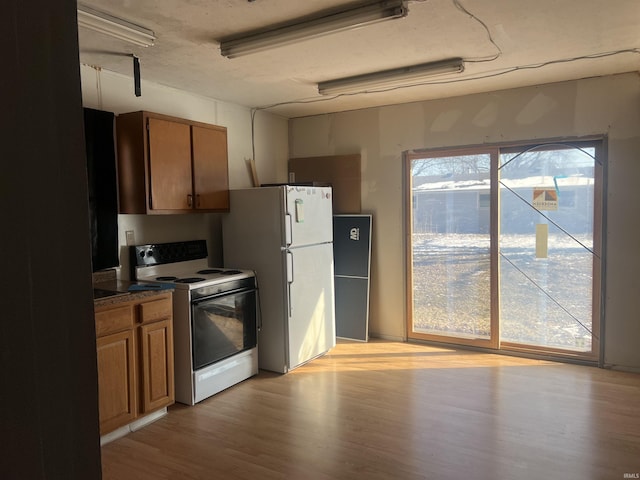 kitchen with white appliances, dark countertops, light wood-style floors, and brown cabinets