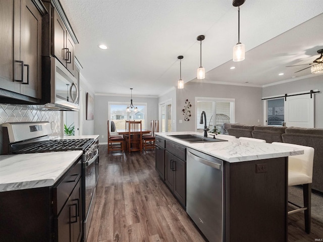 kitchen featuring stainless steel appliances, a sink, ornamental molding, and a barn door