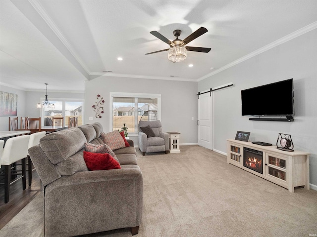 carpeted living room featuring a barn door, ornamental molding, baseboards, and ceiling fan with notable chandelier