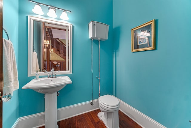 half bathroom with wood finished floors, toilet, and baseboards