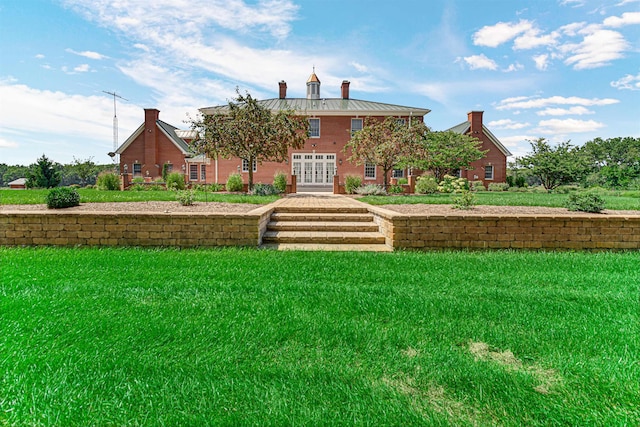 back of house with a standing seam roof, a yard, a chimney, and metal roof