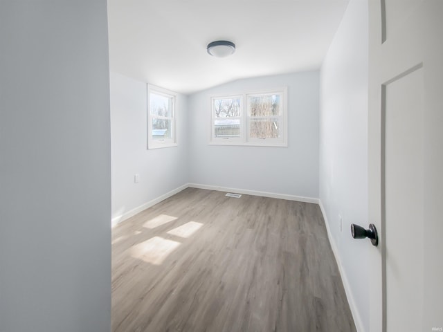 empty room featuring lofted ceiling, baseboards, and wood finished floors