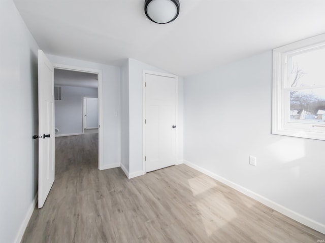 unfurnished bedroom with vaulted ceiling, light wood finished floors, visible vents, and baseboards