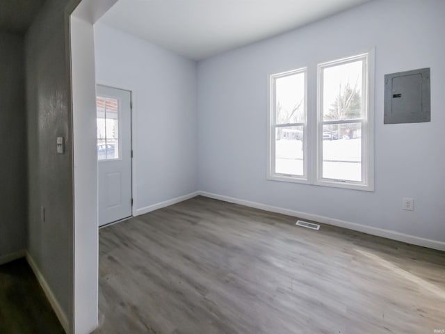 empty room with baseboards, electric panel, visible vents, and wood finished floors