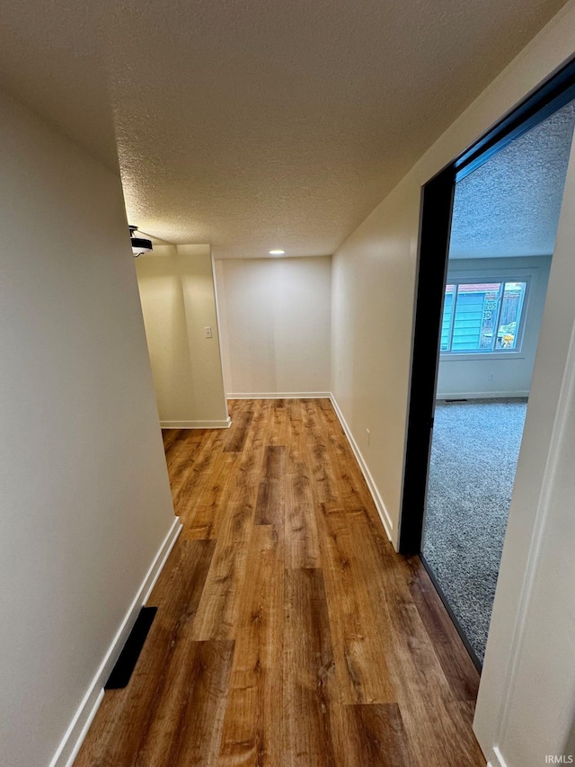 hall with baseboards, a textured ceiling, and wood finished floors