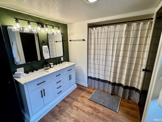 full bathroom with a textured ceiling, double vanity, wood finished floors, and a sink