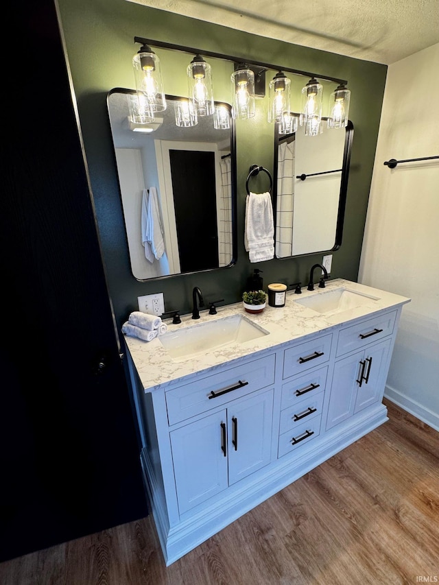 bathroom with a textured ceiling, double vanity, wood finished floors, and a sink