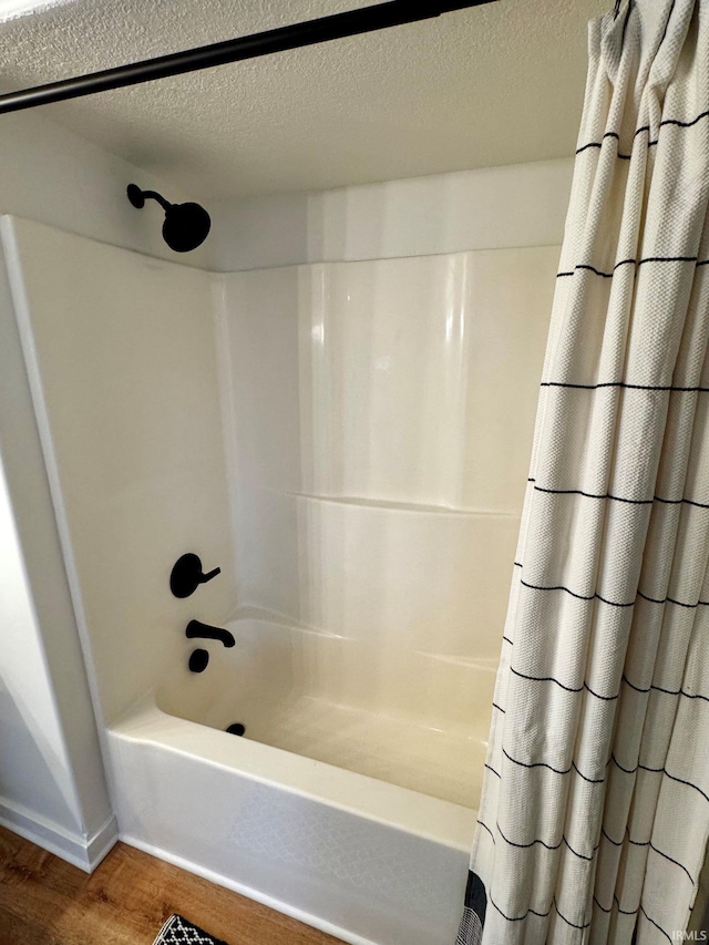 bathroom with shower / bathtub combination with curtain, a textured ceiling, and wood finished floors