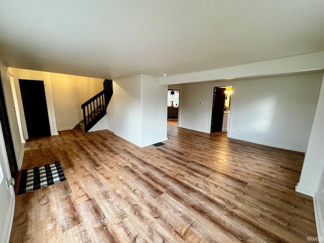 spare room featuring stairs, a textured ceiling, wood finished floors, and baseboards