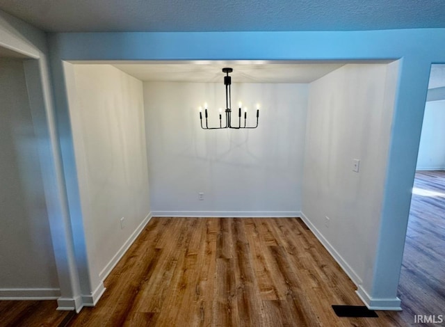 unfurnished dining area featuring baseboards, a textured ceiling, wood finished floors, and a notable chandelier