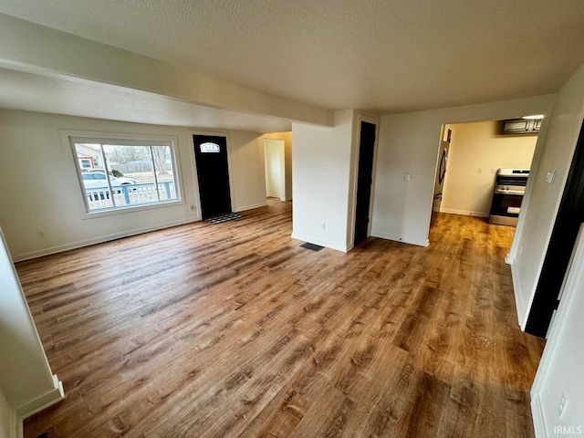 unfurnished living room featuring baseboards, a textured ceiling, visible vents, and wood finished floors