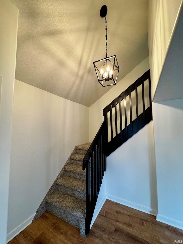 stairway with baseboards, a textured ceiling, wood finished floors, and a notable chandelier