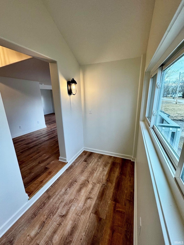 spare room with vaulted ceiling, baseboards, and wood finished floors