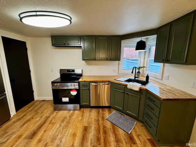 kitchen with wood counters, a sink, stainless steel appliances, light wood-type flooring, and green cabinetry