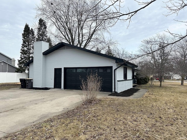 view of side of home with concrete driveway, a chimney, and an attached garage