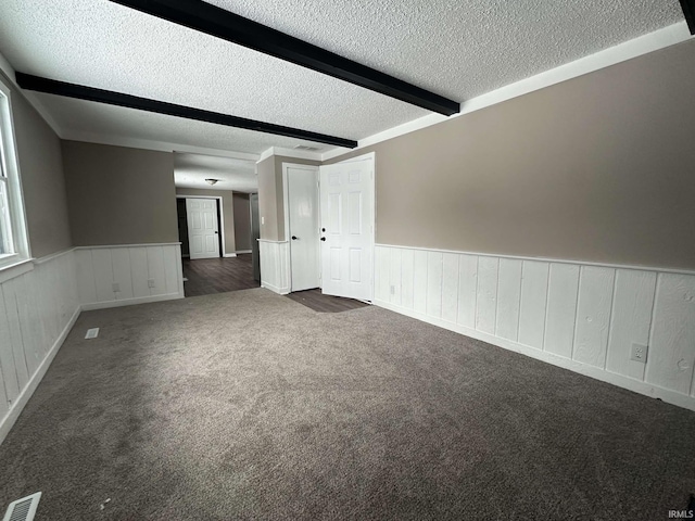 spare room featuring a textured ceiling, visible vents, wainscoting, beamed ceiling, and dark carpet