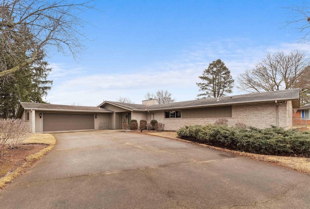 ranch-style house featuring a garage, brick siding, driveway, and a chimney