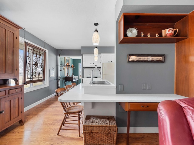 kitchen with light wood-style flooring, a sink, light countertops, freestanding refrigerator, and decorative light fixtures