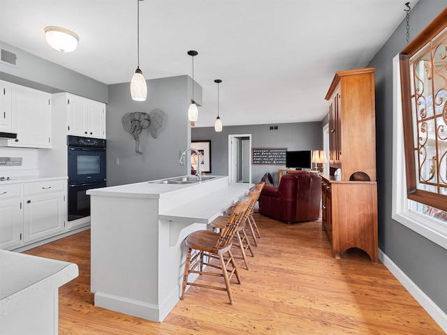 kitchen with dobule oven black, a sink, open floor plan, light countertops, and light wood finished floors