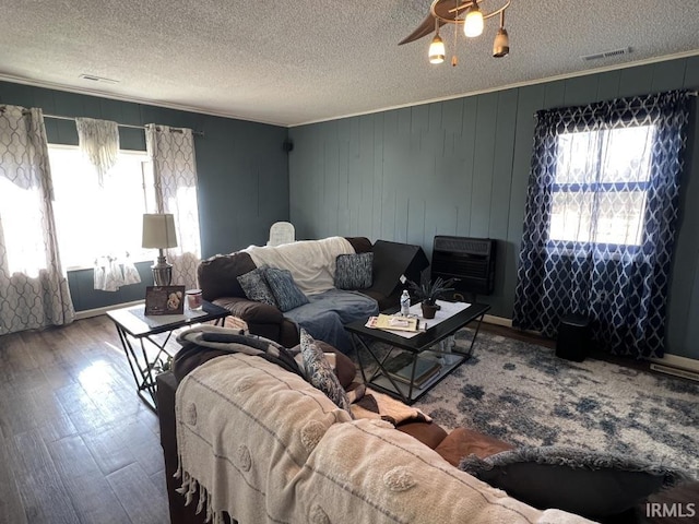 living area with a textured ceiling, ceiling fan, wood finished floors, heating unit, and crown molding