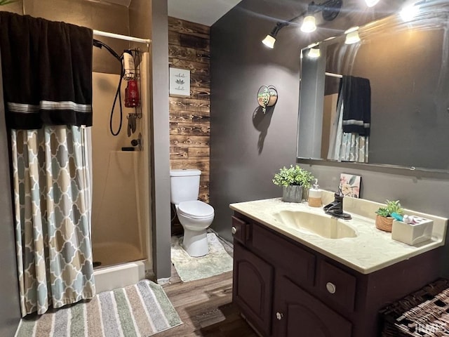 bathroom featuring toilet, wooden walls, wood finished floors, vanity, and a stall shower