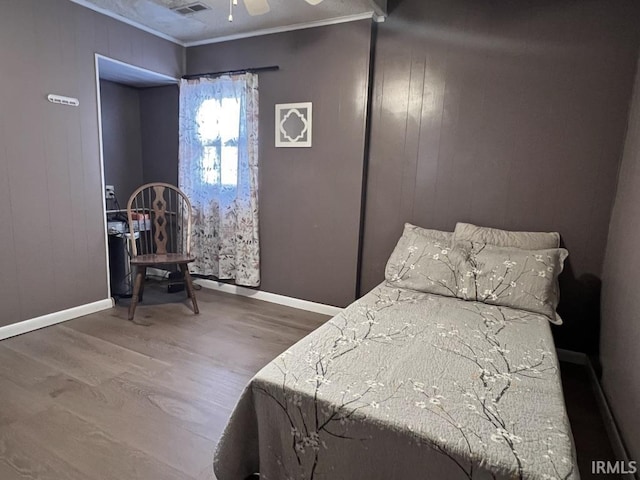 bedroom featuring baseboards, wood finished floors, visible vents, and crown molding