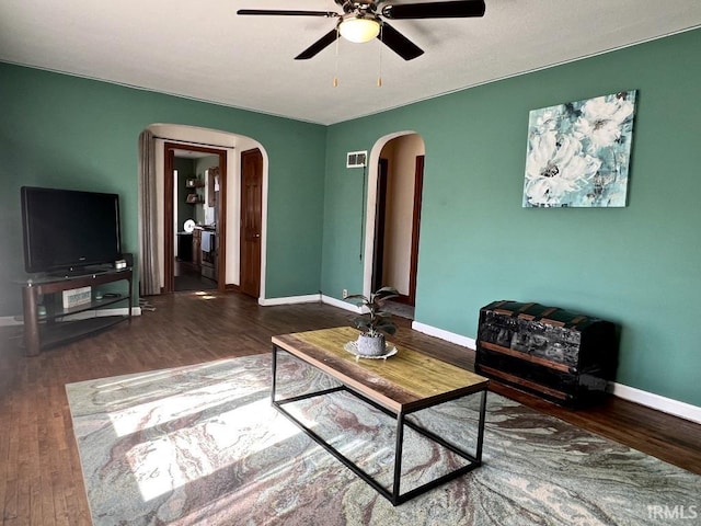 living area with arched walkways, wood finished floors, visible vents, and baseboards