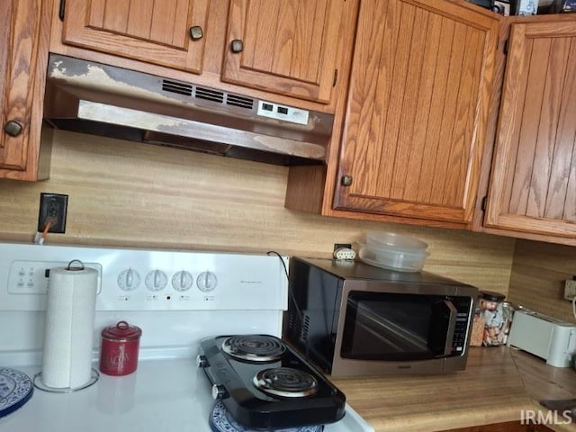 kitchen with brown cabinetry, stainless steel microwave, under cabinet range hood, and tasteful backsplash