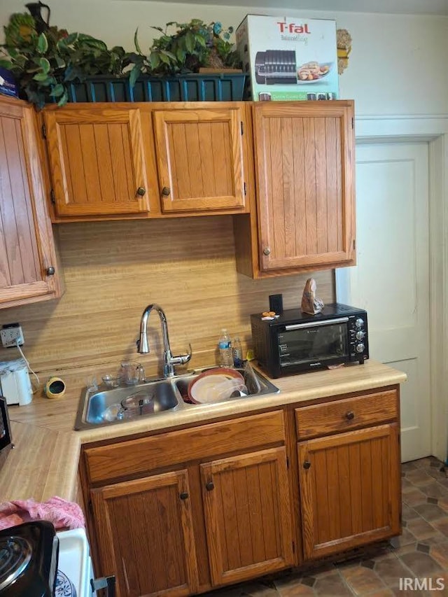 kitchen featuring a toaster, decorative backsplash, stove, light countertops, and a sink