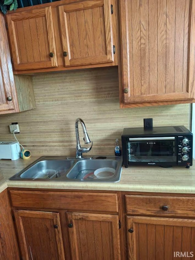 kitchen with brown cabinets, light countertops, a sink, and decorative backsplash