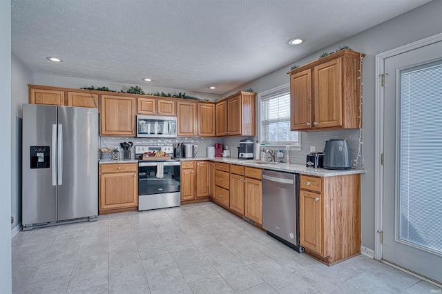 kitchen with brown cabinets, backsplash, light stone countertops, stainless steel appliances, and a sink