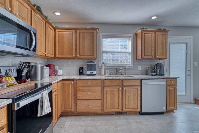 kitchen with stainless steel appliances, a sink, visible vents, decorative backsplash, and brown cabinetry