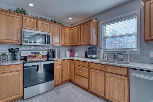 kitchen with decorative backsplash, appliances with stainless steel finishes, light tile patterned flooring, a sink, and light stone countertops