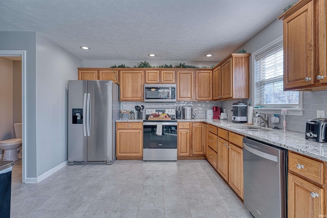 kitchen featuring a sink, baseboards, appliances with stainless steel finishes, light stone countertops, and brown cabinetry