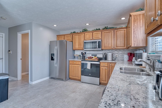 kitchen with a sink, baseboards, appliances with stainless steel finishes, light stone countertops, and tasteful backsplash