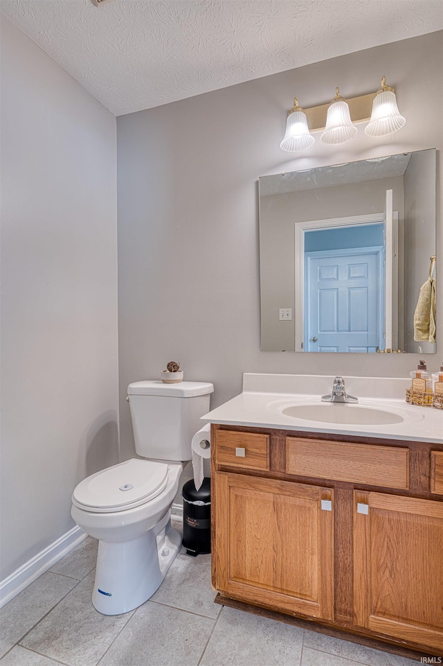 bathroom with toilet, vanity, a textured ceiling, tile patterned flooring, and baseboards