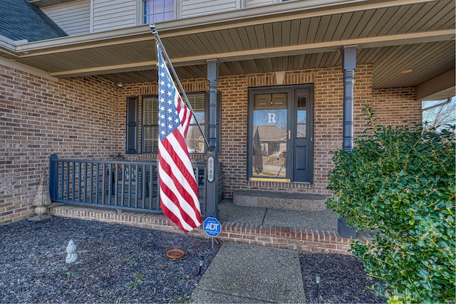 entrance to property featuring a porch and brick siding