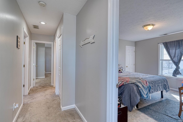 hallway featuring light carpet, a textured ceiling, visible vents, and baseboards