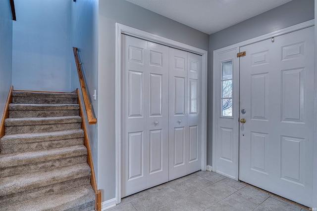 foyer entrance featuring stairs, light tile patterned floors, and baseboards