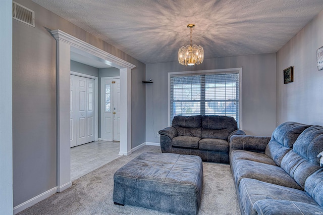 carpeted living area featuring baseboards, a textured ceiling, visible vents, and a notable chandelier