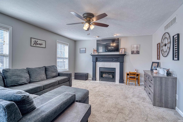 carpeted living area featuring baseboards, visible vents, ceiling fan, a textured ceiling, and a fireplace