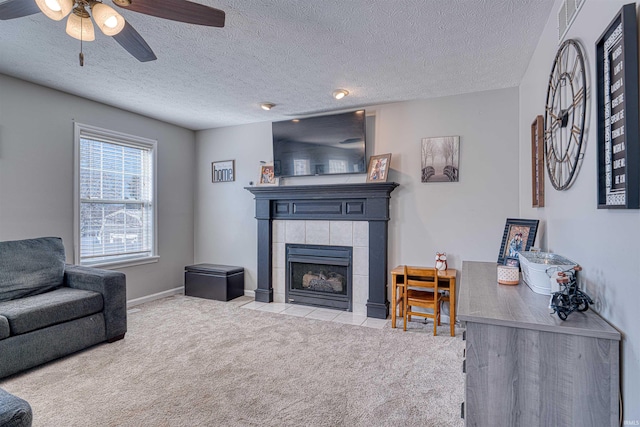 carpeted living area featuring ceiling fan, baseboards, a textured ceiling, and a tile fireplace