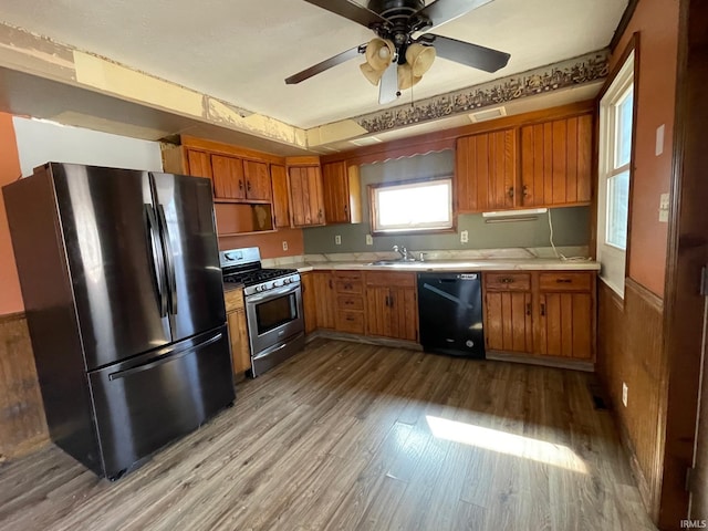 kitchen with black appliances, brown cabinetry, wood finished floors, and light countertops