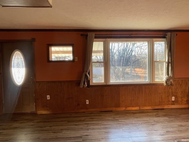 entryway featuring a wainscoted wall, wood walls, a textured ceiling, and wood finished floors